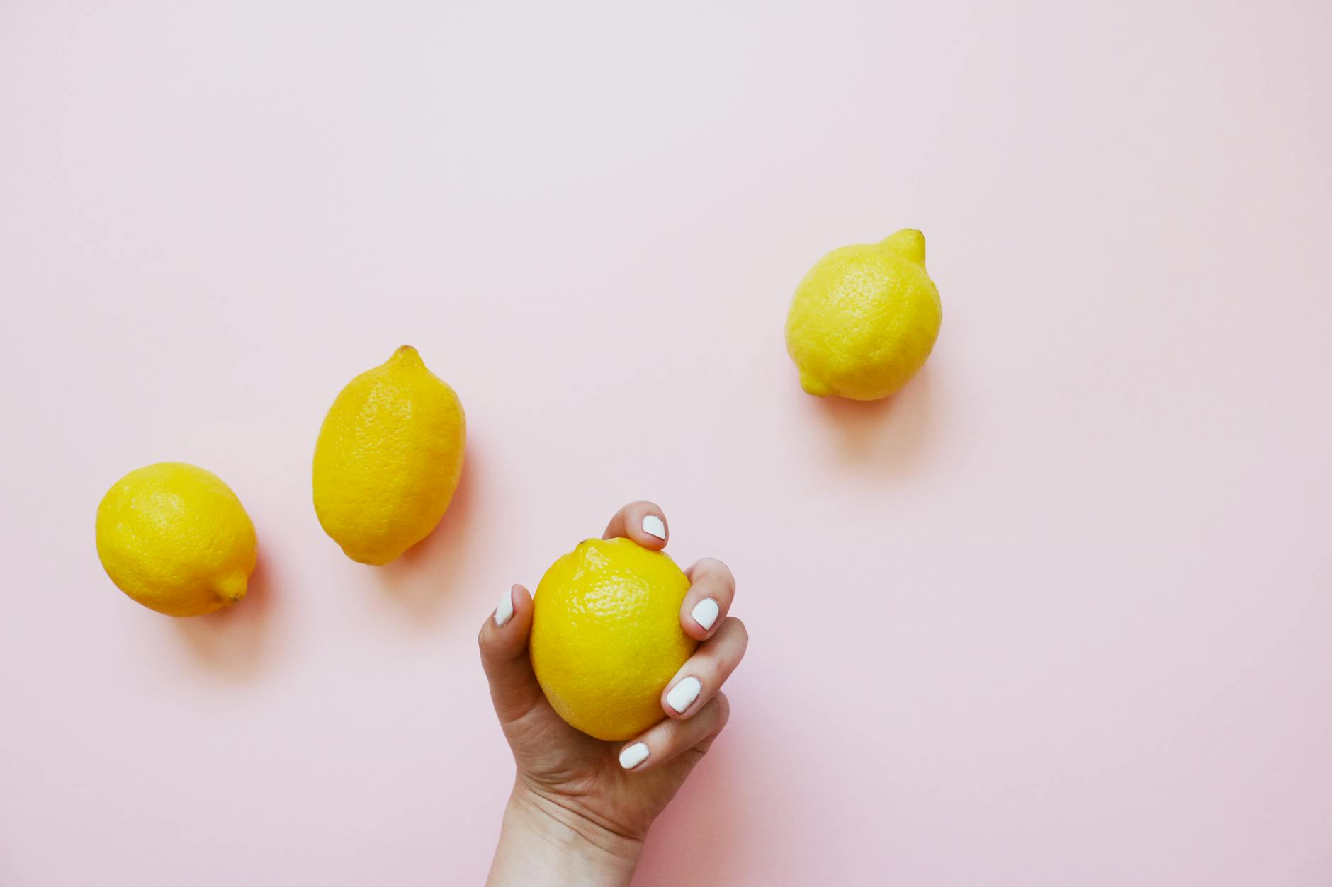 Hand holding fresh lemons on soft pink background, symbolizing natural pleasure and vitality