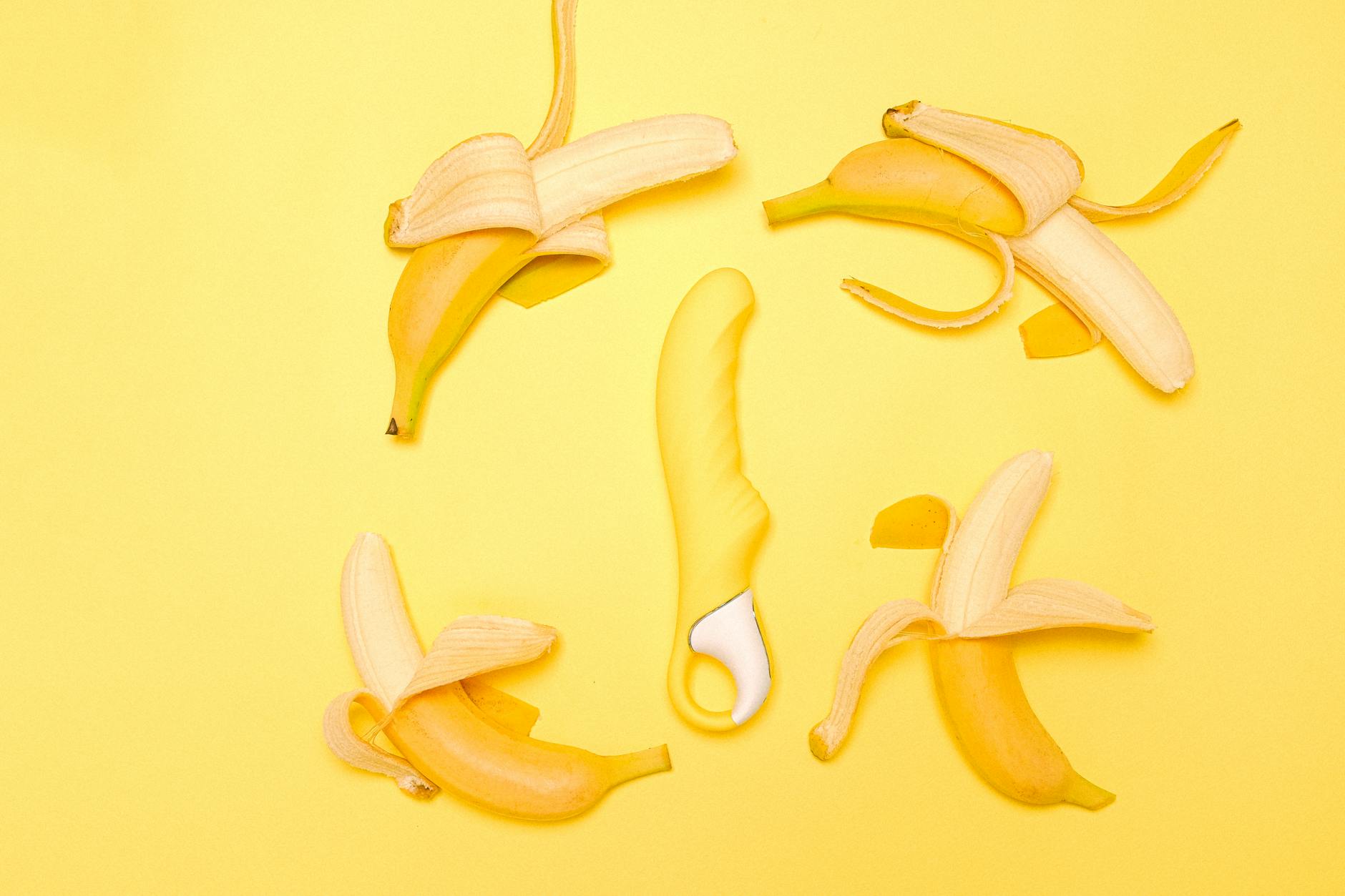 Yellow lemon vibrator surrounded by fresh lemons on a bright yellow surface