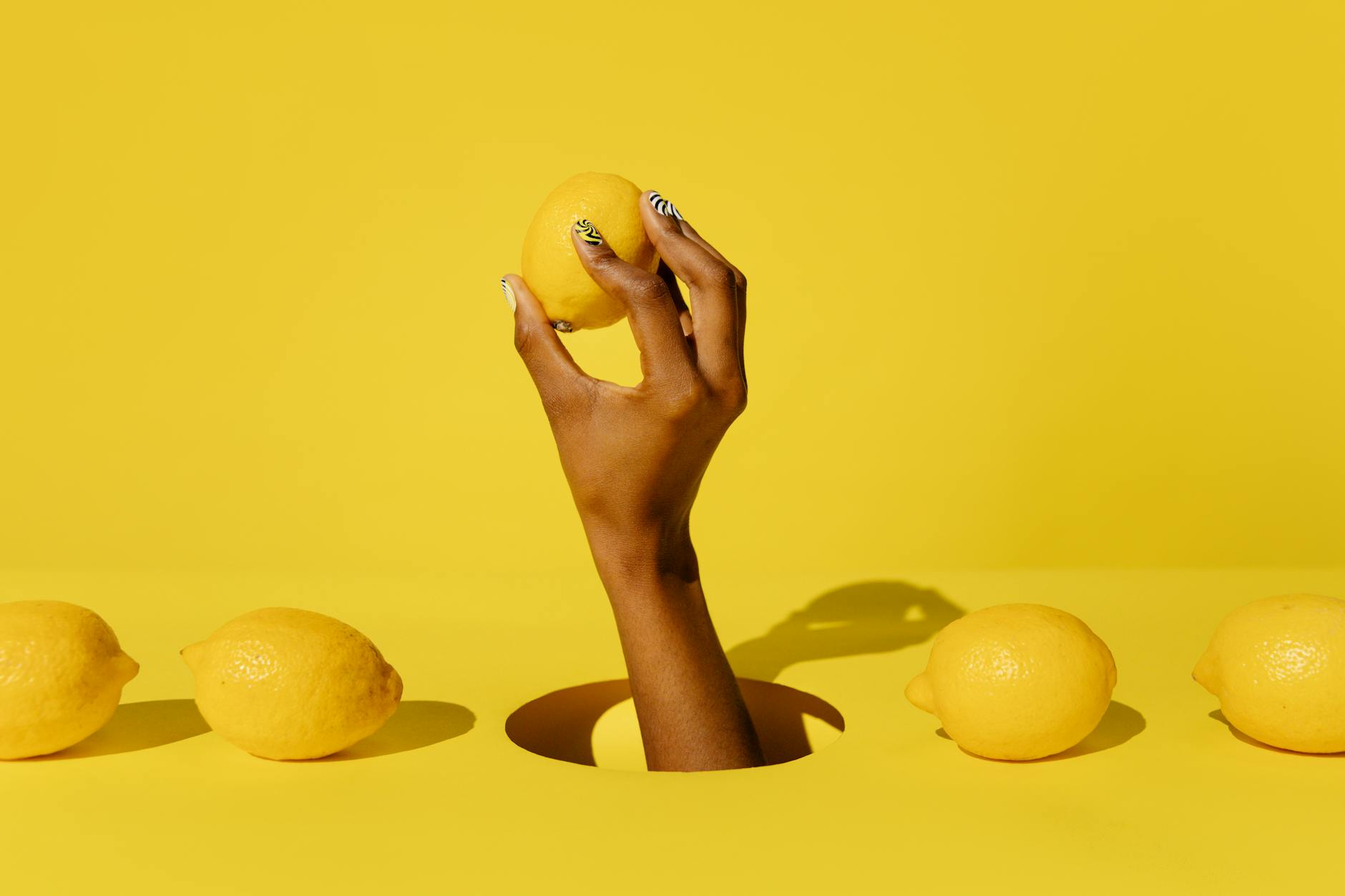 A hand holding a fresh lemon against a bright yellow background, symbolizing renewal and fresh starts