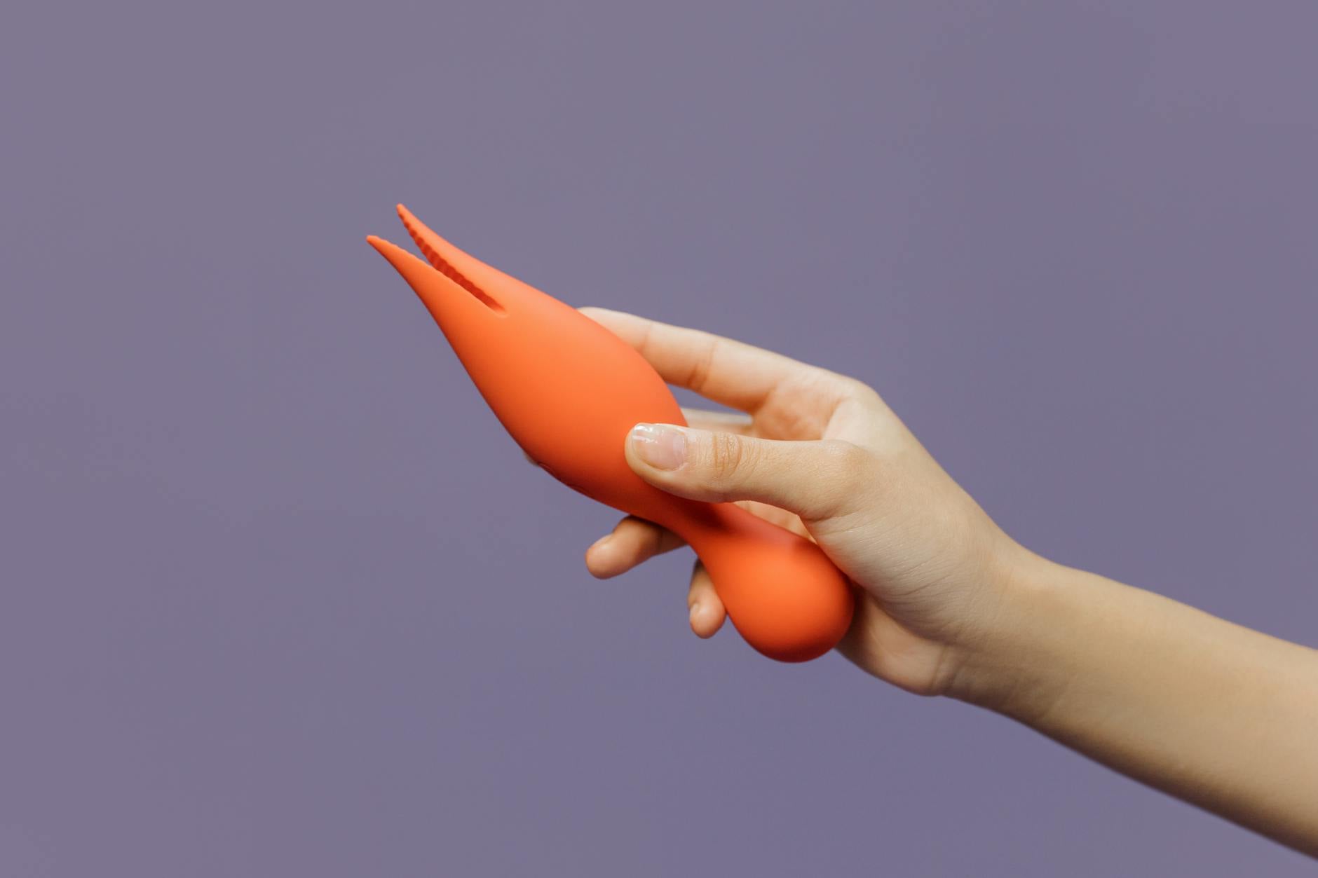 A close-up of a hand holding a lemon-colored vibrator against a minimalistic purple backdrop, showcasing modern sensuality