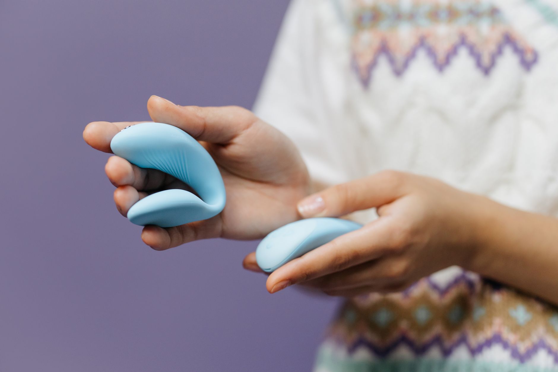 A hand holding a sleek blue vibrator against a purple background.