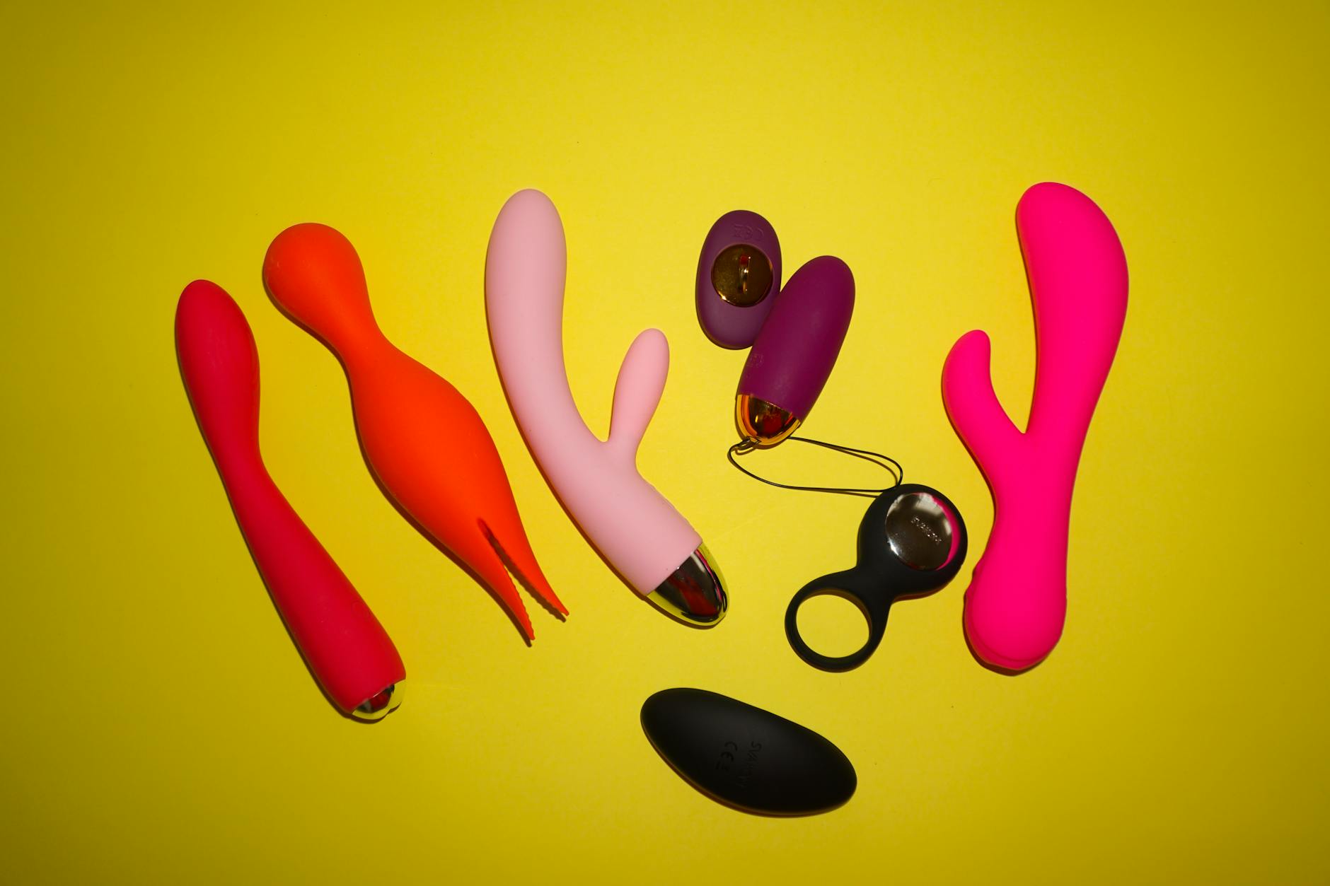 黄色い背景にカラフルなセックストイが並ぶスタジオ写真